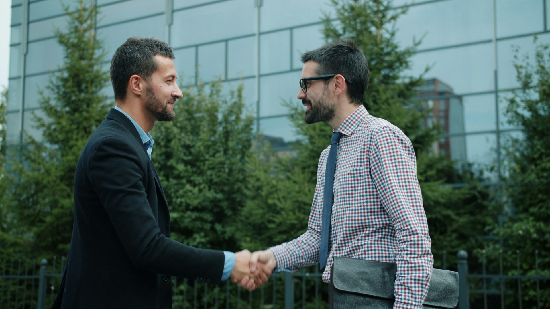 Two businessmen shaking hands outside an office building.